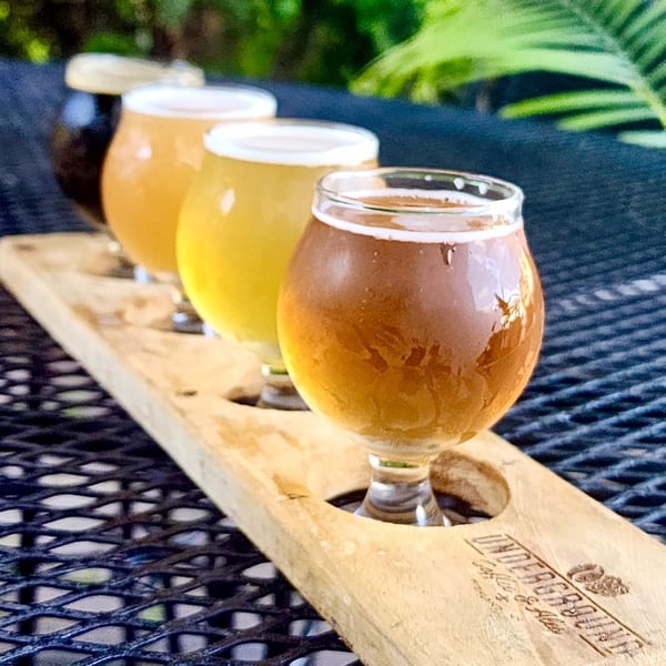 A flight of four beers on a wooden paddle from Underground Coffee & Ales on an outdoor table.